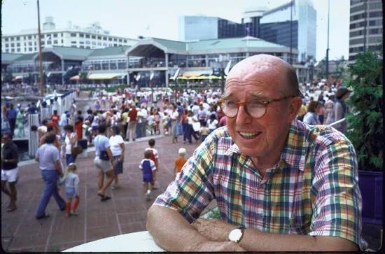 James Rouse photographed at Baltimore's Inner Harbor with Harborplace and crowds in the background.